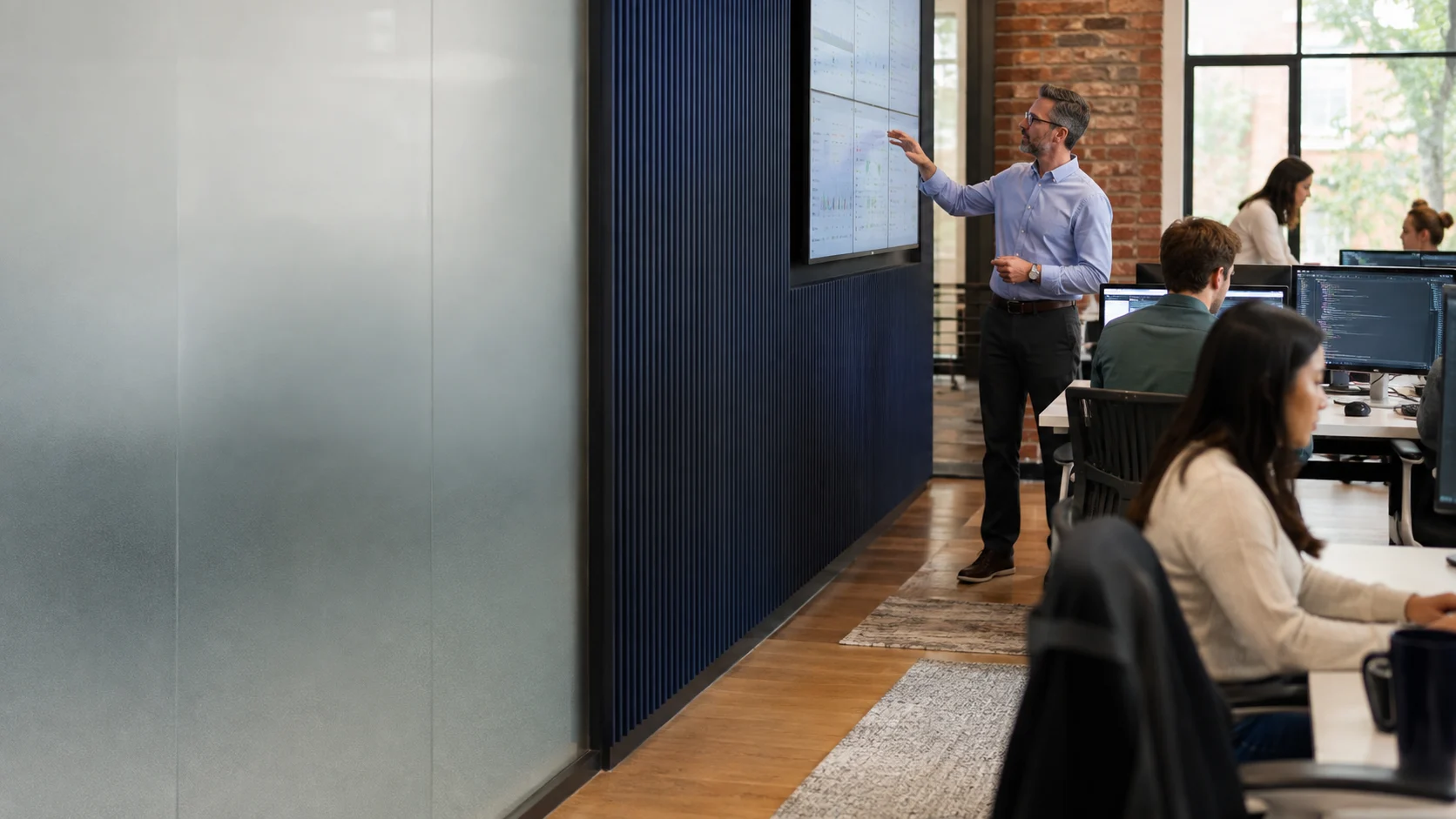 Technology operations leader monitoring product systems while software teams work in a modern office.